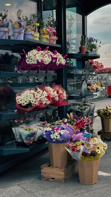 An outdoor display of fresh floral arrangements and bouquets at a flower shop, featuring a variety of colorful flowers including white daisies, pink lilies, purple irises, and mixed seasonal blooms wr