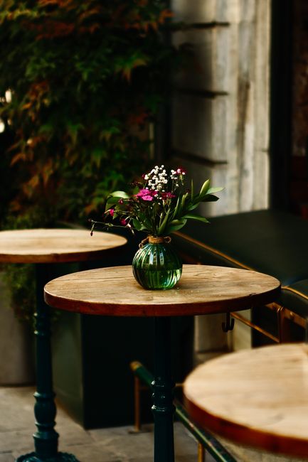 A floral arrangement featuring a variety of fresh flowers, including pink, white, and purple blossoms, complemented by green foliage, and arranged in a small, round, green glass vase with a decorative